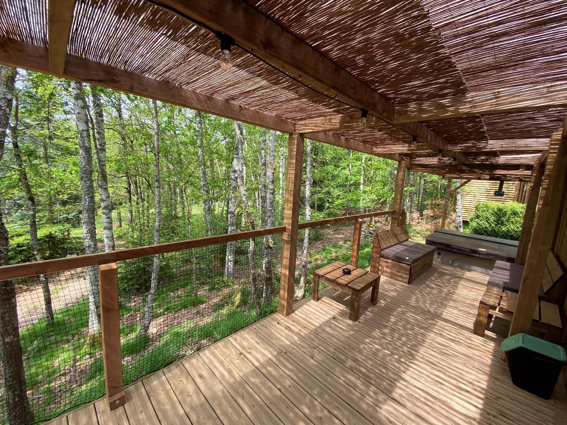 Een houten terras met een pergola, een bank en een tafel.