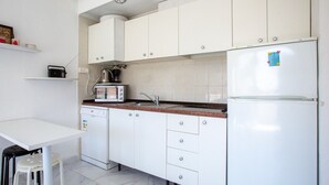 Uma cozinha compacta com armários brancos, lava-louças embutida, torradeira e frigorífico.