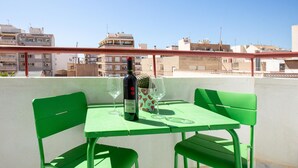 Terraço no telhado com mesa e cadeiras verdes, uma garrafa de vinho e um copo.