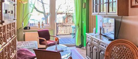 Una habitación con una pared verde, un mueble de madera con un televisor, una silla roja y una silla de mimbre.