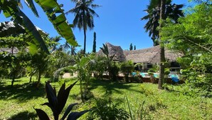 Una località turistica tropicale con un edificio a tetto di paglia, una piscina e vegetazione lussureggiante.