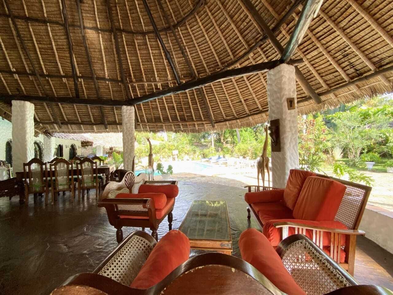 A covered outdoor seating area with wooden furniture and a thatched roof.