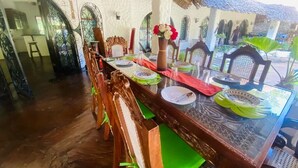 Zona pranzo con tavolo in vetro, sedie di legno e tetto di paglia.