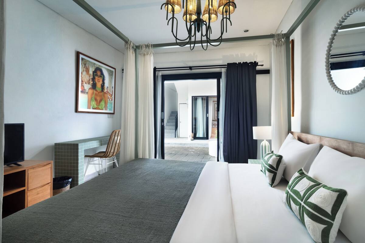 Habitación de hotel con una cama grande, televisión, una silla y un cuadro en la pared.