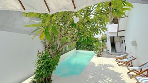 A pool area with a clear blue pool, surrounded by white walls and wooden deck chairs. - Berawa Nest Canggu (Tibubeneng)