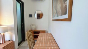 A narrow hallway with a tiled floor, a wooden bench, a wall-mounted mirror, and a framed picture. - Berawa Nest Canggu (Tibubeneng)