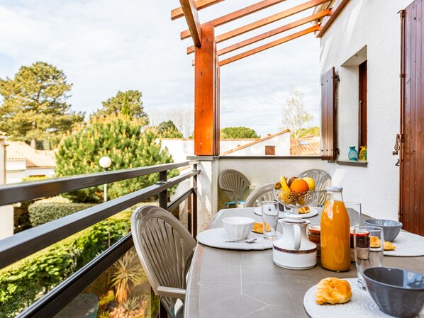 A balcony with a table set for breakfast, including fruits, bread, and beverages.