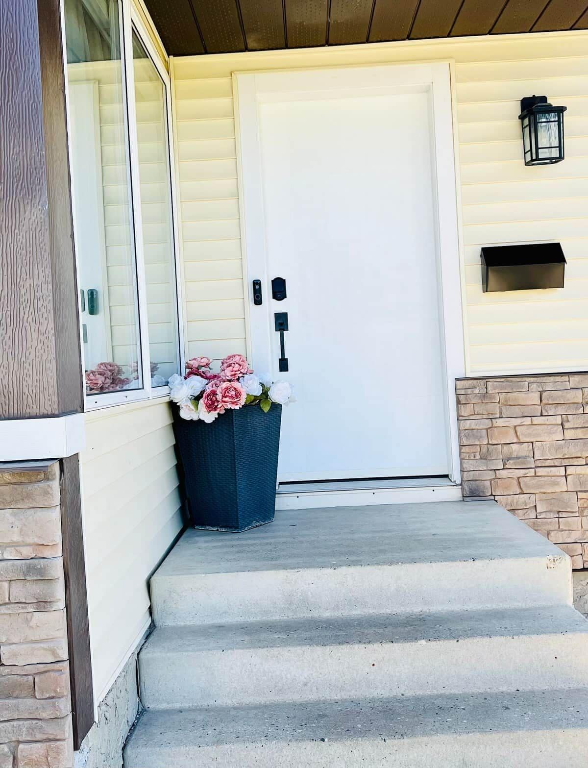 A front entrance with a white door, a small porch, and a flower pot with flowers.