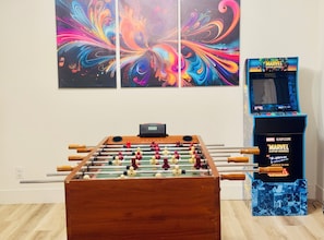 Una mesa de fútbol de mesa, una pared con arte abstracto y una máquina arcade Marvel Capcom.