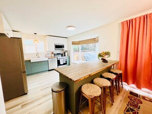 A modern kitchen with a central island, bar stools, and a view of the outdoors.