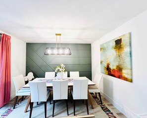 A dining area with a modern table, chairs, a vase of flowers, and a large abstract painting on the wall.