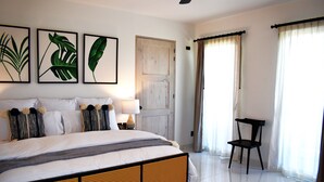Ein Schlafzimmer mit einem Bett, Kissen, einem Sessel, einer Tür und gerahmten Kunstwerken an der Wand.