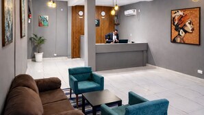 En modern hotellobby med en receptionsdisk, en sittgrupp med soffor och fåtöljer samt konstverk på väggarna.