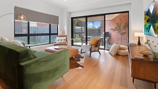 Una sala de estar moderna con un sofá verde, una mesa de centro de madera y un comedor con pared de ladrillo y ventanas grandes.