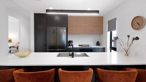 Una cocina moderna con una isla central, armarios negros y de madera, un refrigerador de acero inoxidable y un reloj en la pared.