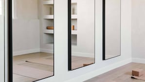 Ein modernes Zimmer mit drei großen Spiegeln an der Wand, Holzboden und einer integrierten Regaleinheit.