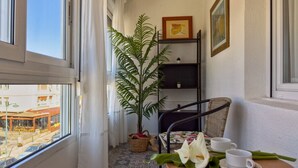 A balcony with a potted plant, a wicker chair, a small table with cups and a flower, and a view of a building outside. - Apto 3 Dormitorios Somo - Peñasblancas 30801 (Somo)