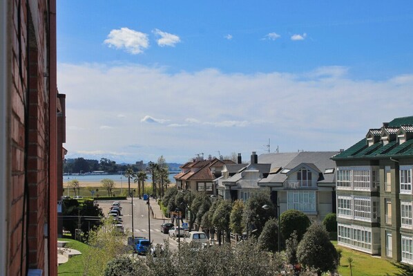 A coastal residential area with a view of the sea, houses with green roofs, and a clear sky.