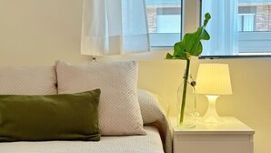 A neatly made bed with a green pillow, a bedside table with a lamp, and a plant. - Apto 3 Dormitorios Somo - Peñasblancas 30801 (Somo)