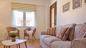 A living room with a beige sofa, two wicker chairs, a small white table, and a potted plant. - Apto 3 Dormitorios Somo - Peñasblancas 30801 (Somo)