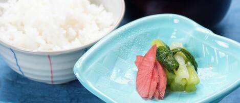 A bowl of white rice, a black bowl with a green vegetable, and a blue plate with a pink slice of meat and green vegetables.