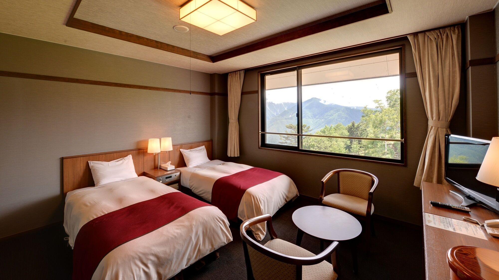 Une chambre d’hôtel avec deux lits, un bureau avec une chaise, une télévision et une fenêtre donnant sur la montagne.