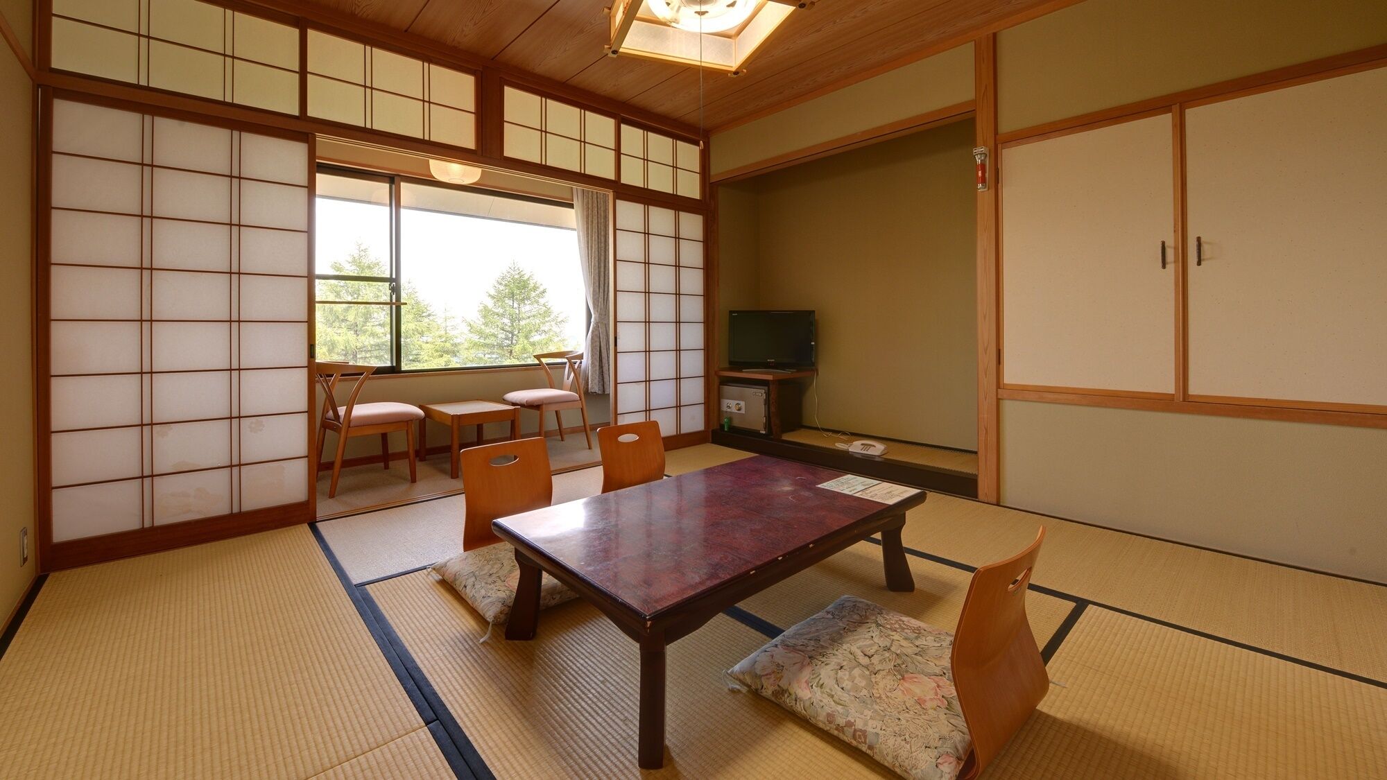 Une pièce de style japonais traditionnel, avec un sol recouvert de tatamis, une table basse, des chaises, un téléviseur et des portes coulissantes.