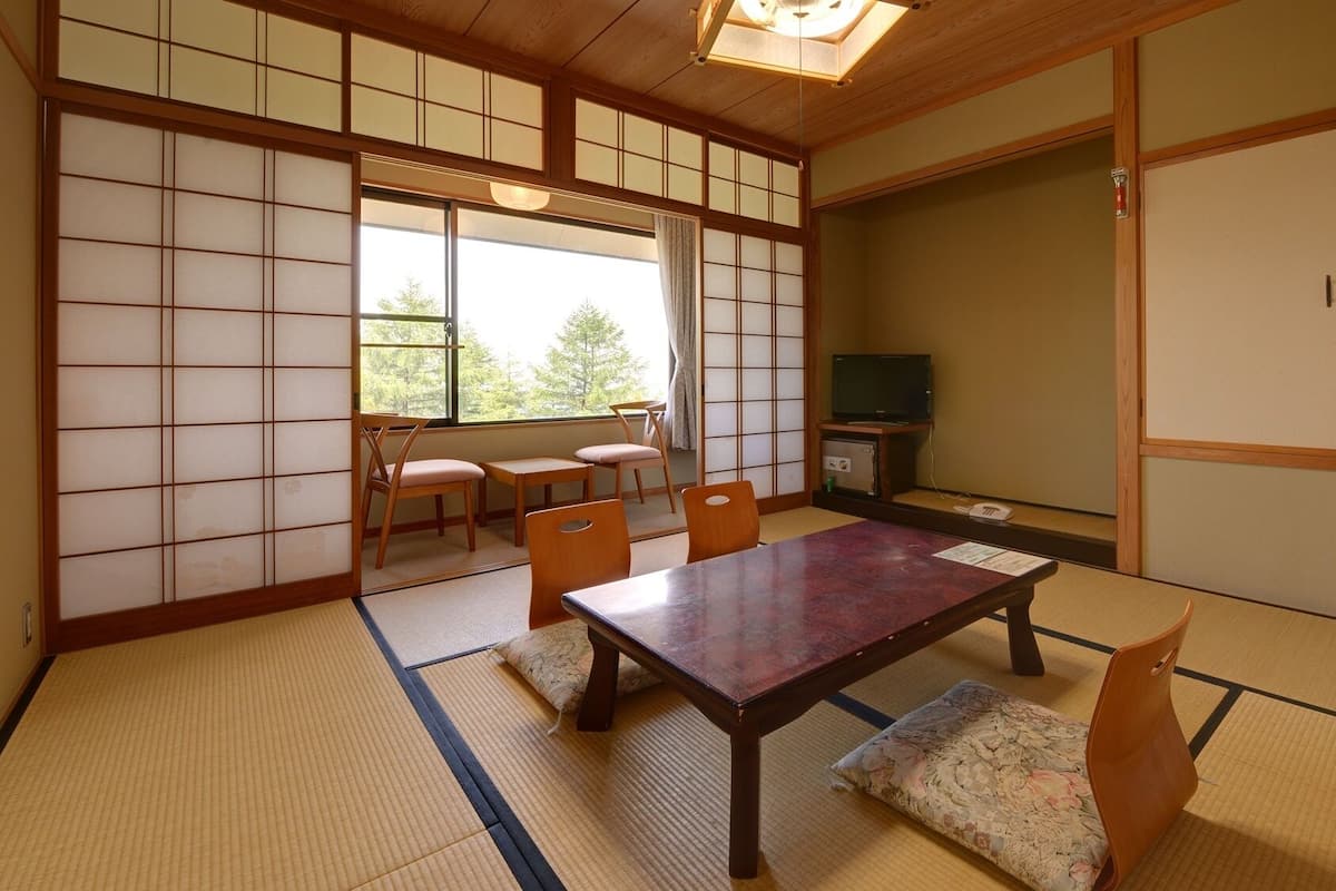 A traditional Japanese room with tatami flooring, a low table, chairs, a television, and sliding doors.