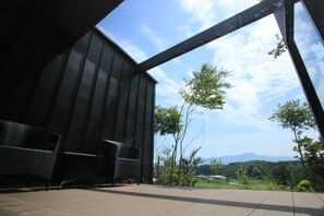A modern building with a large glass window and a patio area with outdoor furniture. - Shirokane no Mori (Kikuchi)