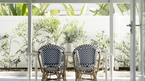 Un espace patio avec deux chaises et une table, entouré de plantes et d’une clôture blanche.
