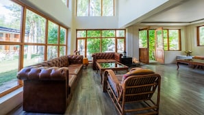 A spacious room with large windows, a leather sofa, a wooden table, and a wicker chair. - Hotel Shambhala Resort (Leh)