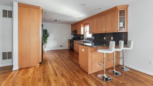 A modern kitchen with wooden cabinets, a black countertop, and three bar stools. - Luxury NY Home with Free Parking (White Plains)