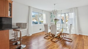A modern kitchen with wooden cabinets, a glass dining table, and a bar stool. - Luxury NY Home with Free Parking (White Plains)