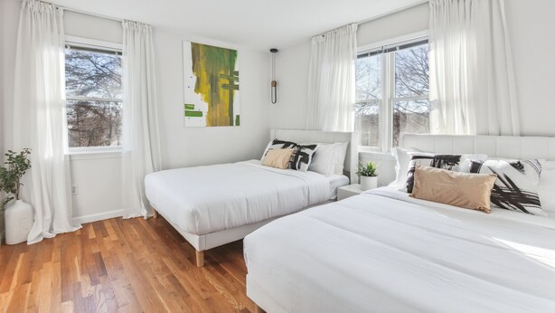 A bedroom with two beds, white bedding, and a large window with curtains. - Luxury NY Home with Free Parking (White Plains)