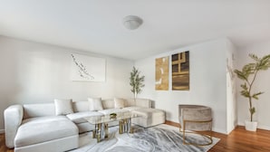 A modern living room with a sectional sofa, a glass coffee table, and a marble rug. - Luxury NY Home with Free Parking (White Plains)