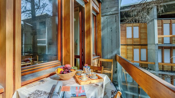 A balcony with a table set for breakfast, wooden furniture, and a view of neighboring buildings. - Slalom 73 few Steps From Skiing (Bardonecchia)