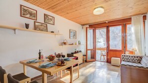 A cozy living room with a wooden ceiling, a dining area with a wooden table and chairs, and a sofa. There are framed pictures on the wall and a window with curtains. - Slalom 73 few Steps From Skiing (Bardonecchia)