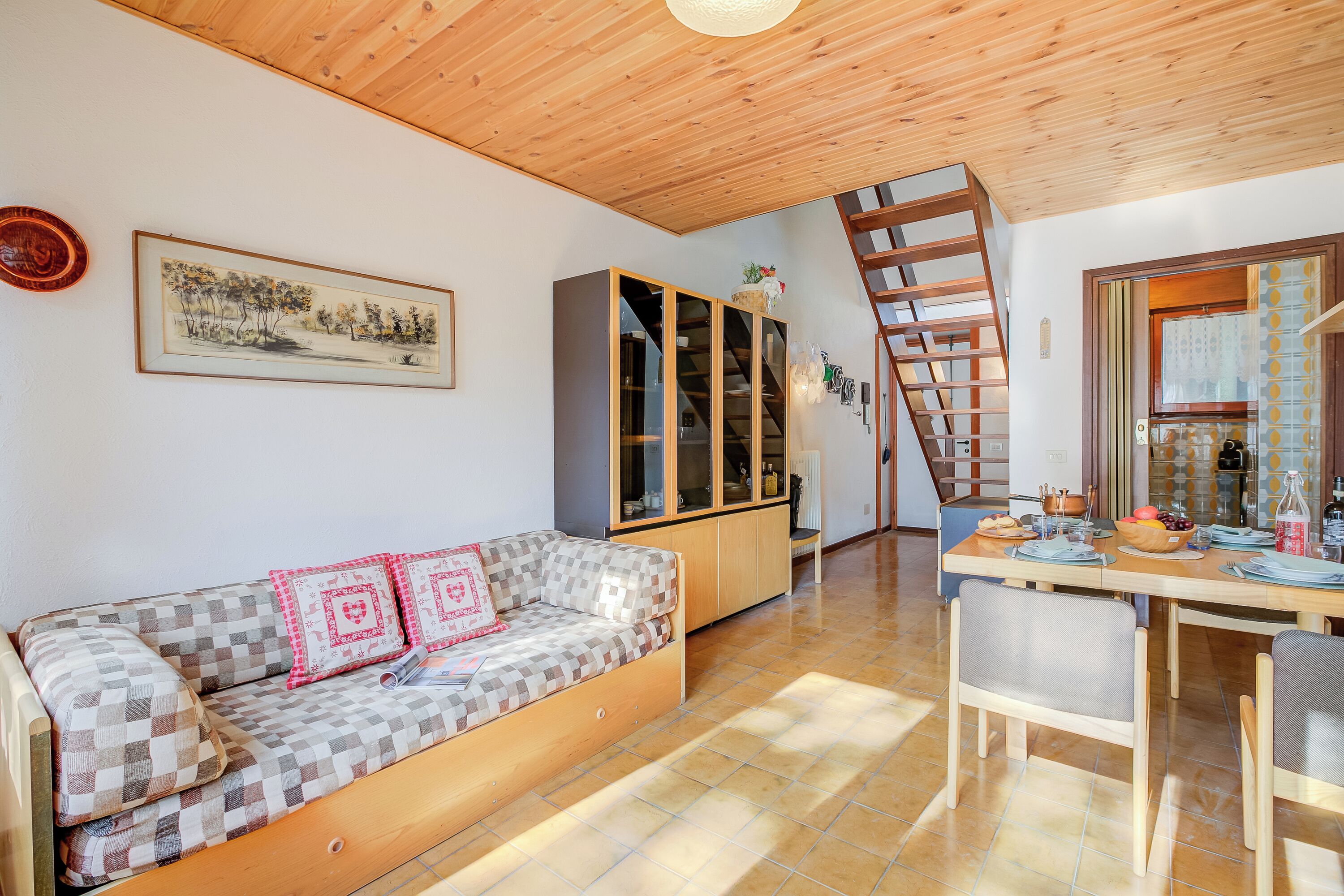 Uma sala de estar aconchegante com um sofá quadriculado, um armário de madeira e uma mesa de jantar com cadeiras.