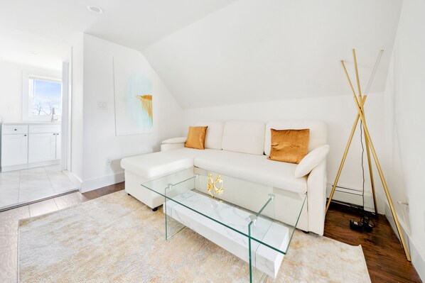 A modern living room with a glass coffee table, white sofa with orange cushions, and a floor lamp. - NY Luxury Apt Free Parking in PRIME Area (Yonkers)