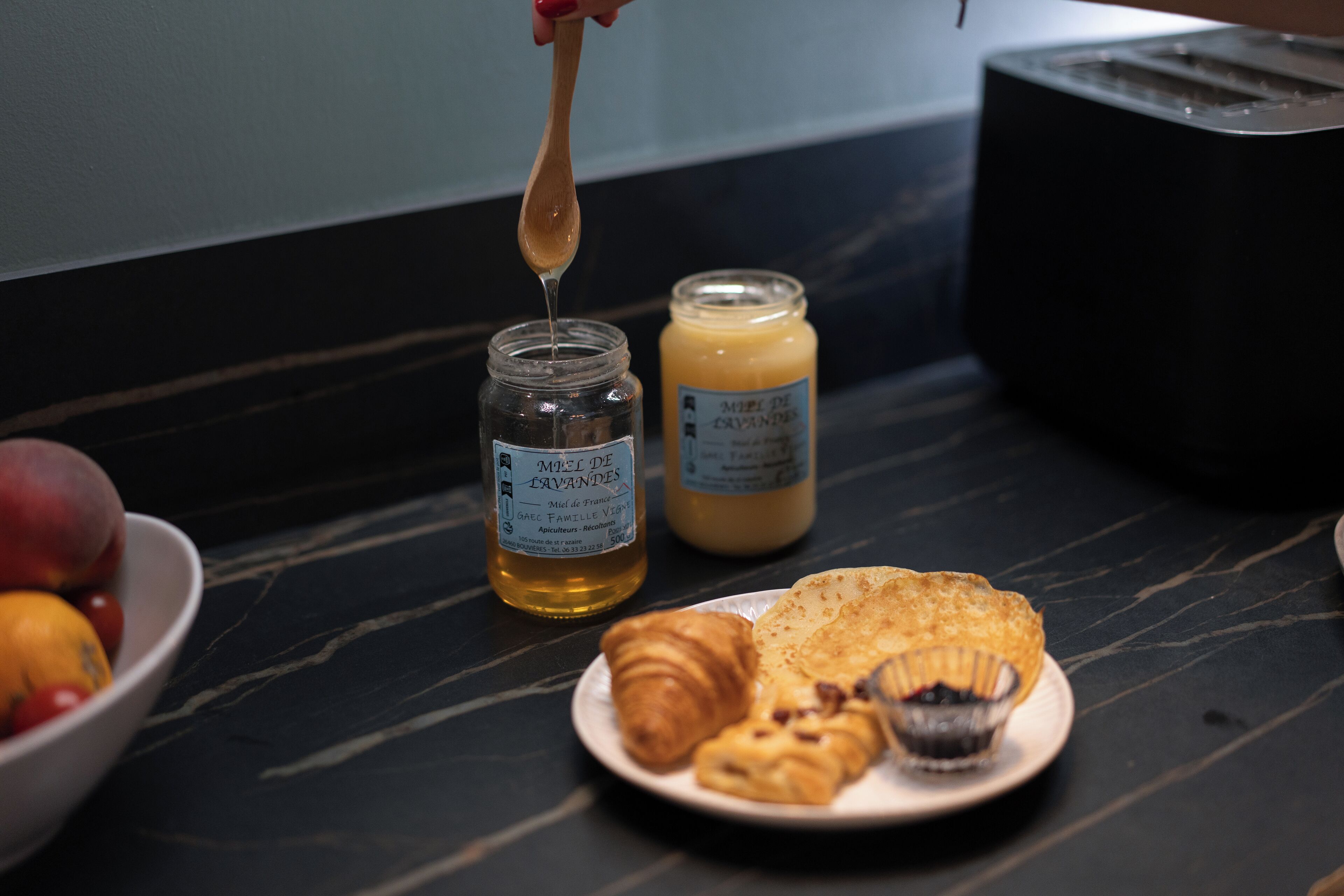 En morgenmadsopsætning med et fad croissanter, en skål frugt og to krukker med honning.