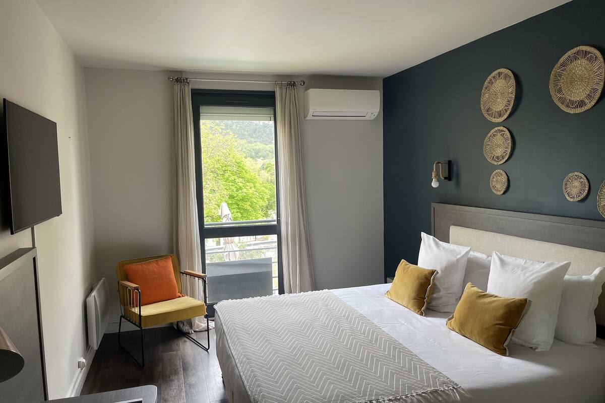 A hotel room with a bed, a chair, a TV, and a window with curtains.