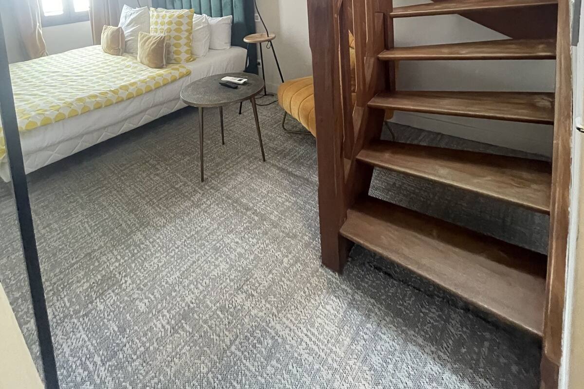 A bedroom with a bed, a small table, a lamp, a sofa, and a wooden staircase.