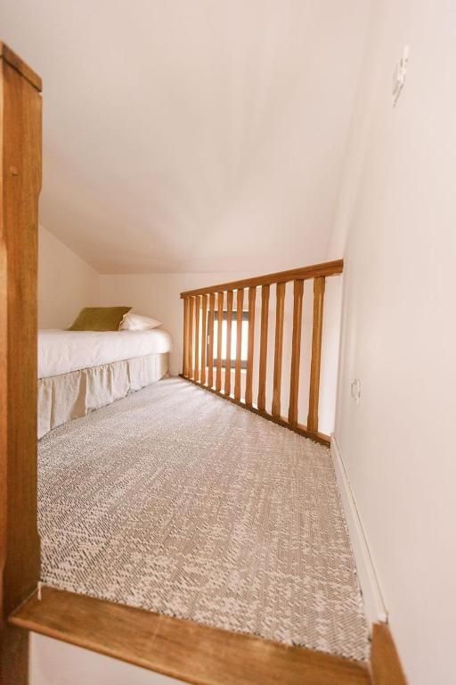 Eine enge Treppe mit Holelllaufstäben führt zu einem Schlafzimmer mit einem Bett und einem Fenster.