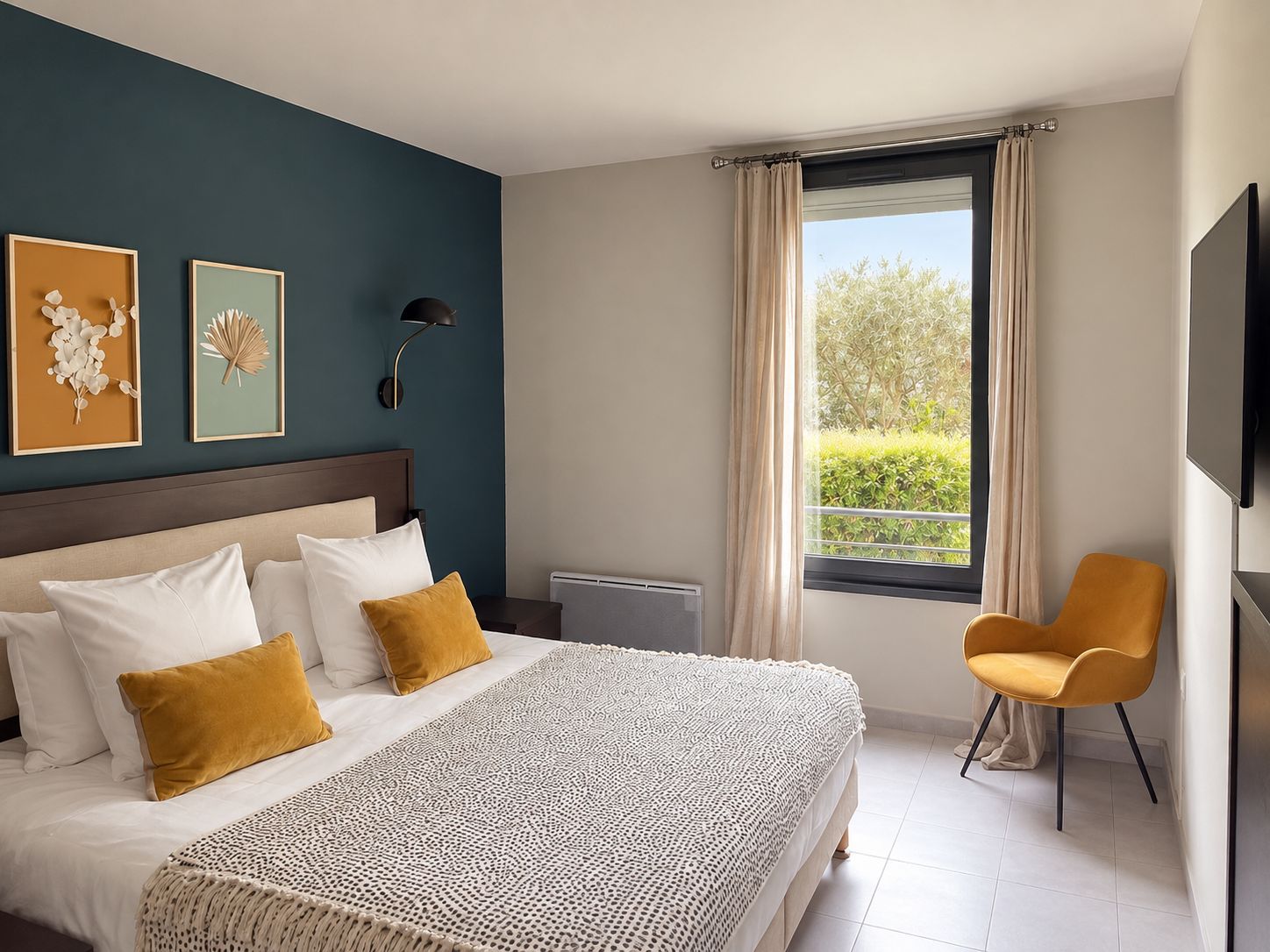 A hotel room with a large bed, a chair, a TV, and artwork on the wall.