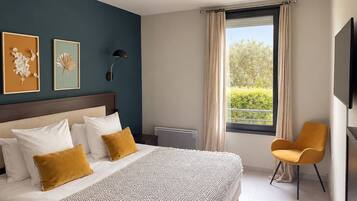 A hotel room with a large bed, a chair, a TV, and artwork on the wall.