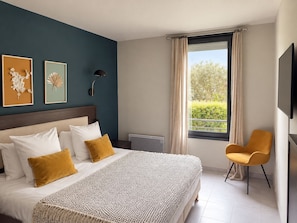 Une chambre d’hôtel avec un grand lit, une chaise, un téléviseur et des œuvres d’art accrochées au mur.