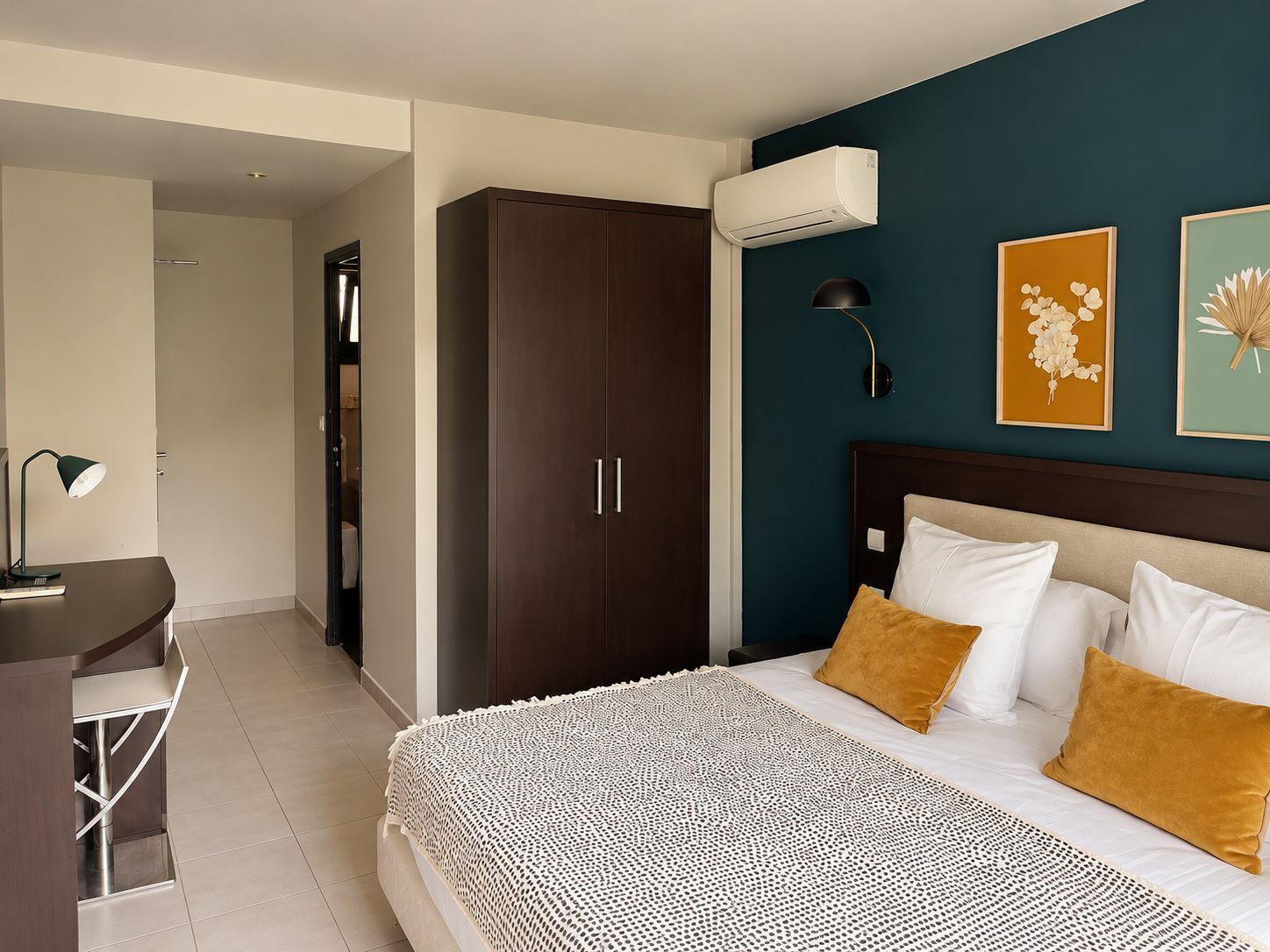 A bedroom with a bed, bedside table, lamp, wardrobe, and wall-mounted air conditioner.