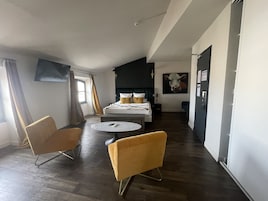 Una habitación de hotel moderna con una cama, dos sillones amarillos, una mesa redonda y un cuadro grande en la pared.