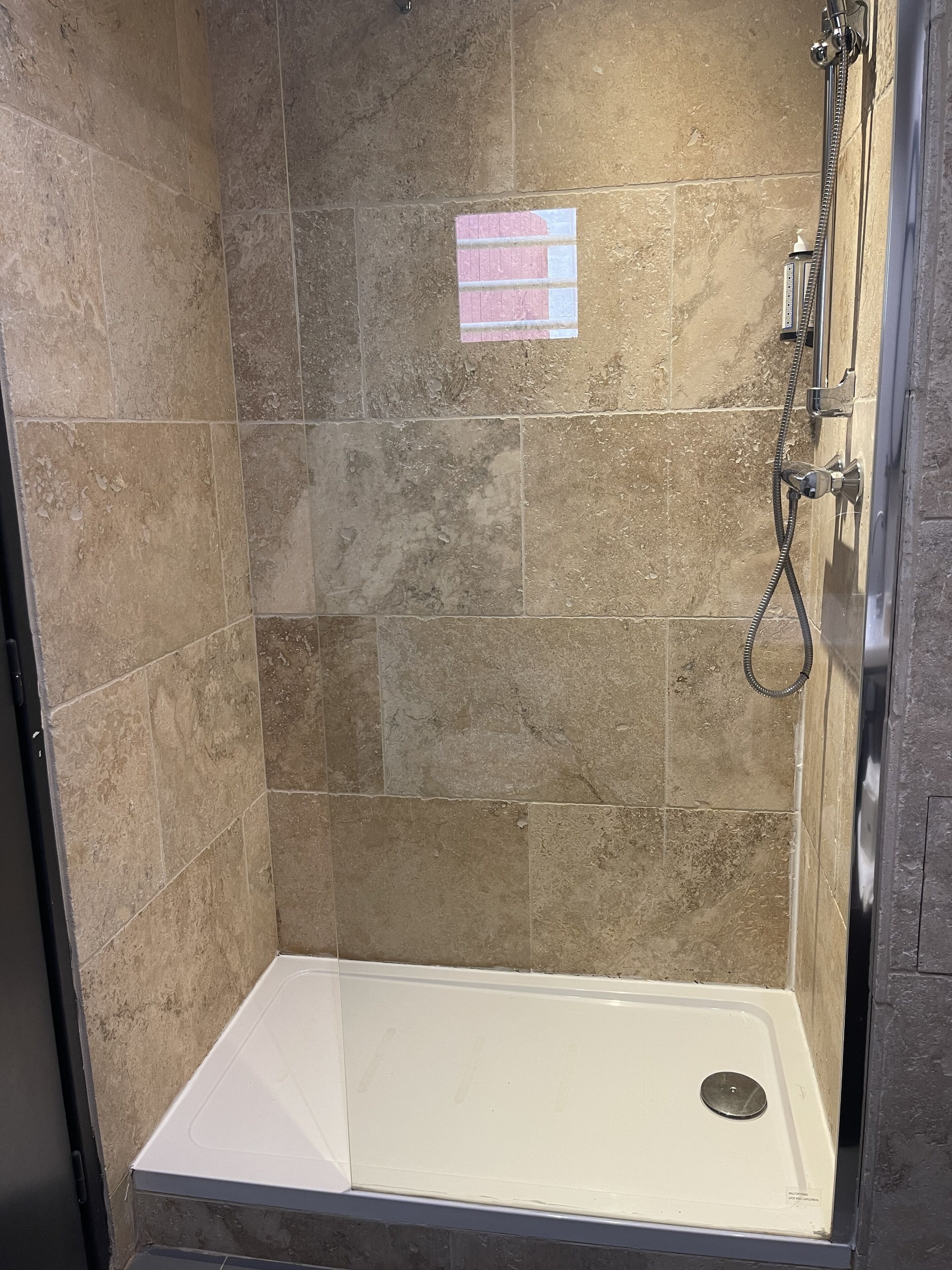 A shower area with a tiled wall, a showerhead, and a white shower seat.