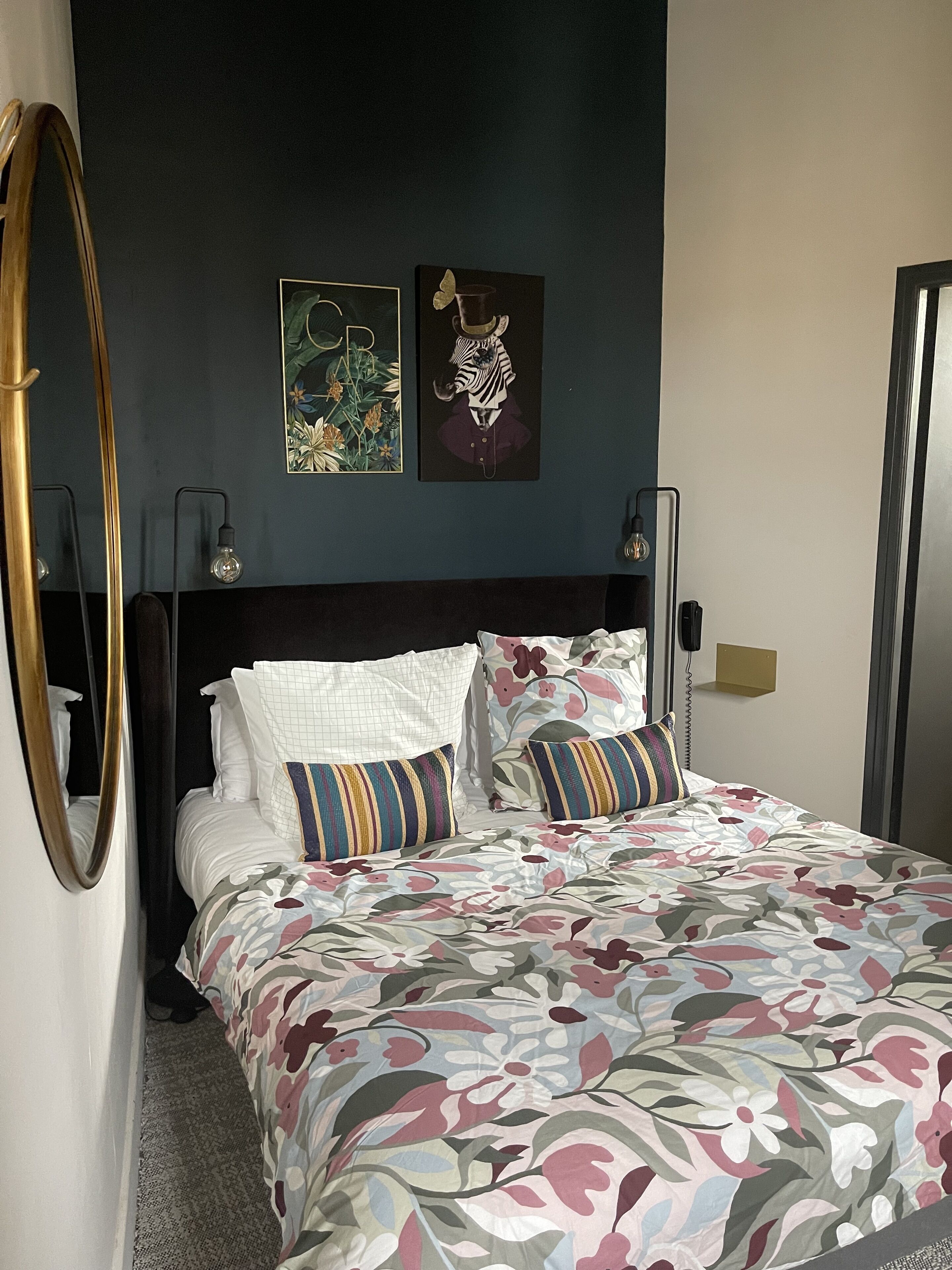 A neatly made bed with floral bedding, a dark headboard, and two wall-mounted light fixtures.